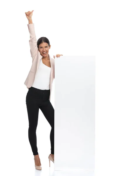 空の板の横に立つピンクのジャケットの幸せな女性の全身写真 空気中の腕を保持し スタジオで白を背景に親指を作ります — ストック写真