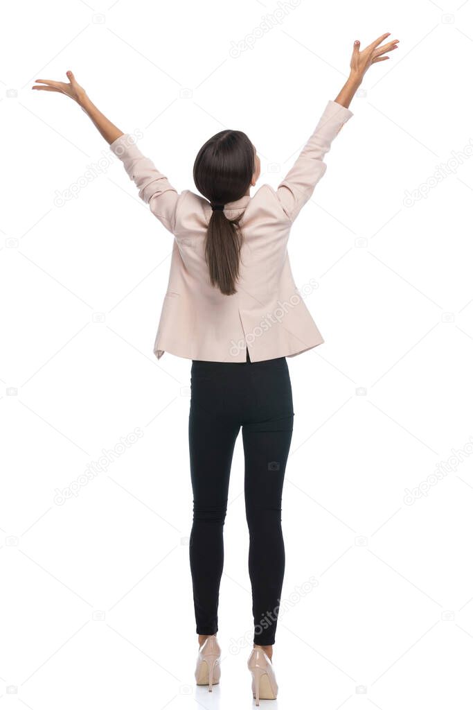 enthusiastic businesswoman in pink jacket holding hands in the air and celebrating, cheering victory and standing isolated on white background in studio
