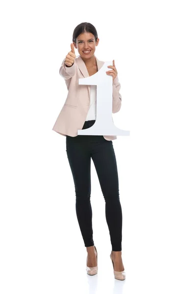 穿着粉色夹克 面带微笑 做手势 在演播室举着头号牌的漂亮年轻姑娘 — 图库照片