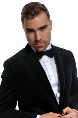 Siyah smokinli zarif bir gencin portresi ve özgüvenle stüdyoda beyaz arka planda poz vermesi.