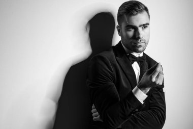 Siyah smokinli, havalı, siyah beyaz bir iş adamı resmi. Papyon takmış, kollarını kavuşturmuş, stüdyoda moda pozu vermiş.