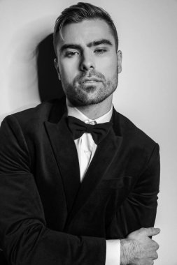 Siyah smokinli genç işadamının siyah beyaz portresi. Stüdyoda dirsek üzerinde duruyor.