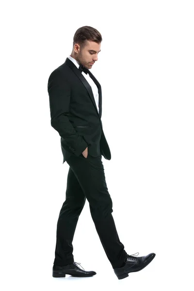 穿着黑色燕尾服的时尚男子手插在口袋里 俯视下方 在工作室的白色背景上独立行走的全身像 — 图库照片