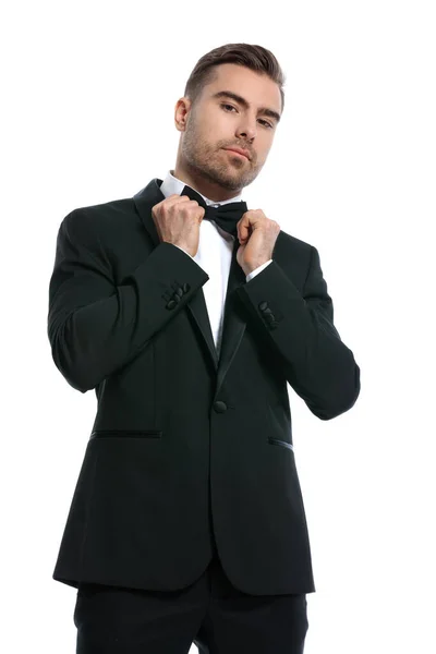 穿着黑色燕尾服的优雅的年轻商人在演播室里修整圆圆的领带 摆出与白色背景隔离的姿势 — 图库照片