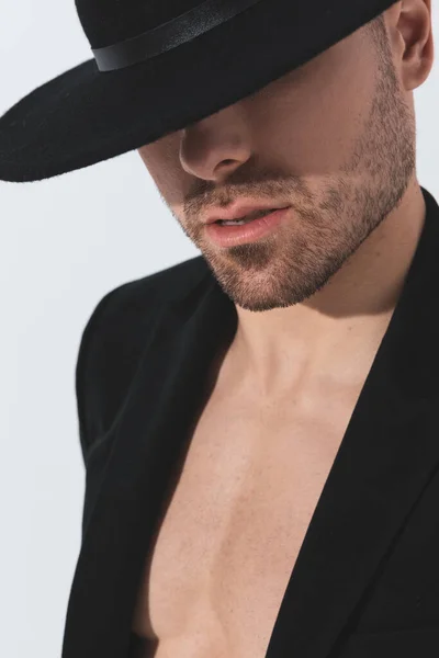 穿着黑色夹克 头戴帽子 在灰色背景中以神秘的方式摆姿势的性感无袖男人的冷静画像 — 图库照片