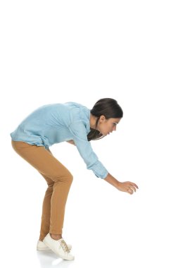 Çekici, sıradan bir kadının beyaz arka plana doğru eğilip bir şeyler yakalamaya çalışmasının yan görüntüsü.