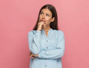 Çekici, sıradan bir kadın çenesini kaşıyor ve bir şeyler düşünüyor ve pembe arka plana bakıyor.