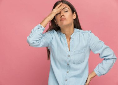 Genç bir kadın kafasına vuruyor ve pembe arka plandaki duruma inanamıyor.