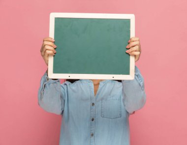 Yeşil bir panonun arkasında yüzünü pembe arka planda saklayan sıradan bir kadın.