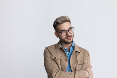 Kot gömlekli, gözlüklü, moda pozu veren ve stüdyoda gri arka planda poz veren zeki bir gencin portresi.