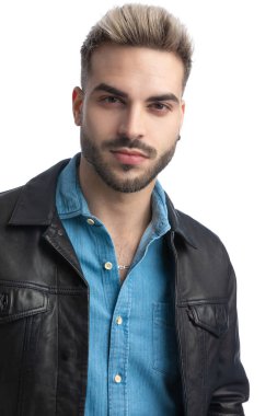 Deri ceketli, gülümseyen ve poz veren havalı genç motosikletçi stüdyoda beyaz arka planda, portrede.