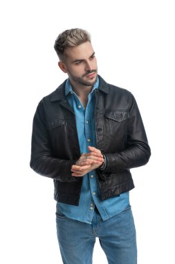 Deri ceketli seksi genç adam avuçlarını ovuyor ve stüdyoda beyaz arka plana karşı poz veriyor.