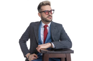 Havalı genç iş adamı kolunu sandalyeye dayayıp başka tarafa bakıyor ve güneş gözlüğü takıyor.