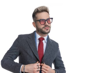 Çekici bir iş adamının portresi ceketini düzenliyor ve beyaz arka plana bakıyor.