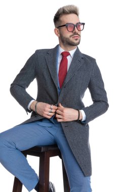 Çekici havalı iş adamı ceketinin düğmesinde el ele tutuşuyor, uzaklara bakıyor ve bir sandalyeye oturuyor. 