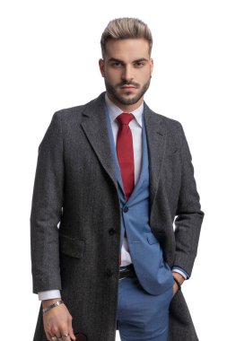 Mavi takım elbiseli, uzun ceketli, el ele tutuşan ve stüdyoda beyaz arka planda poz veren çekici bir genç.