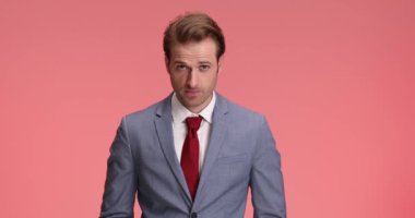 Takım elbiseli yakışıklı adam gülümsüyor ve stüdyoda pembe arka planda durup poz verirken başparmak hareketi yapıyor.