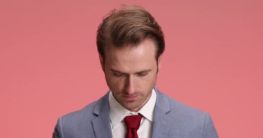 Zarif takım elbiseli ciddi bir iş adamı stüdyoda pembe arka planda poz veriyor.