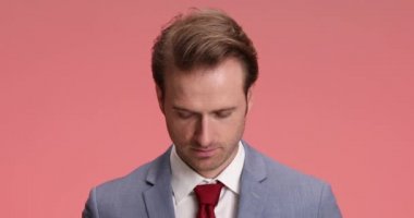 Mavi takım elbiseli gülümseyen genç işadamı stüdyoda pembe arka planda eğlenirken kaşlarını çatıyor ve gülüyor.