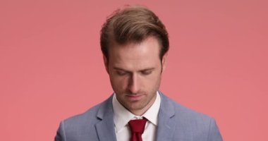 Takım elbiseli genç sakallı adam, stüdyoda pembe arka planda dikilirken korkmuş ve şok olmuş bir ifade takınıyor.