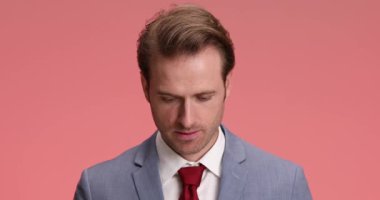 Stüdyoda pembe arka planda dikilirken ve poz verirken parmaklarını gösterip gülümseyen şık takım elbiseli çekici bir iş adamı.