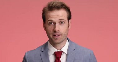 Zarif takım elbiseli gururlu genç adam iyi haberleri alırken aşağıya bakıyor, keyifli hissediyor ve stüdyoda pembe arka planda alkışlıyor.