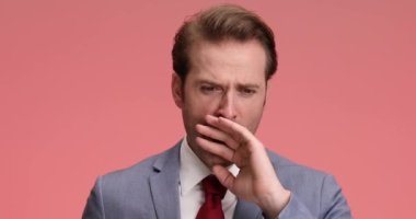 Mavi takım elbiseli yorgun genç adam uykulu ve esniyor, gülümsüyor ve stüdyoda pembe arka planda poz veriyor.