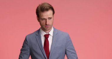 Kendine güvenen, mavi takım elbise ve duruşu düzelten, kravatını gevşeten, kollarını kavuşturan, gülümseyen ve stüdyoda pembe arka planda poz veren zarif bir adam.