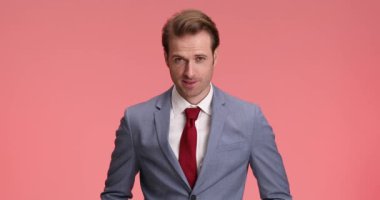 Mavi takımlı çekici, tıraşsız iş adamı aşağıya bakıyor ve gülümsüyor, kollarını kavuşturuyor, çenesine dokunuyor ve stüdyoda pembe arka planı düşünüyor.