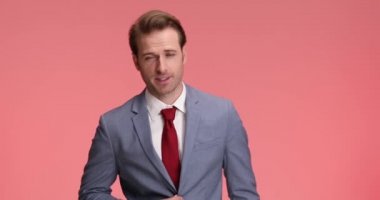 Seksi genç iş adamı şık bir takım elbise iliklerken kendine güvenerek poz veriyor, kollarını kavuşturuyor ve yüzlerine dokunuyor, gülümsüyor ve stüdyoda pembe arka planda ellerini cebine sokuyor.