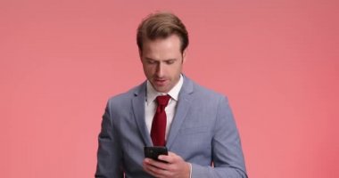 Heyecanlı genç adam elinde telefonla olağanüstü haberler okuyor, havaya yumruk atıyor ve stüdyoda pembe arka planda neşeli çığlıklar atarak kutlama yapıyor.