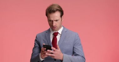 Takım elbiseli kızgın, şık modacı mesajlar okuyor, suratını asıyor, boynunu sıkıyor ve stüdyoda pembe arka planda sallanıyor.