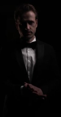 Avuçlarını ovuşturan, yüzüne dokunan, gülen, arka planda iyi vakit geçiren genç bir iş adamının dikey videosu.