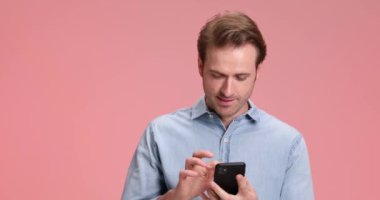 Kot gömlekli, gülümseyen, telefonda konuşan, stüdyoda pembe arka planda gülerken baş parmak hareketi yapan çekici bir adam.