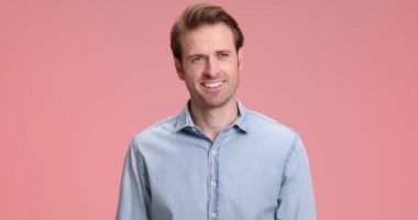 Mavi kot gömlekli mutlu adam yürüyor, gülümsüyor ve stüdyoda pembe arka planda askeri selam veriyor.