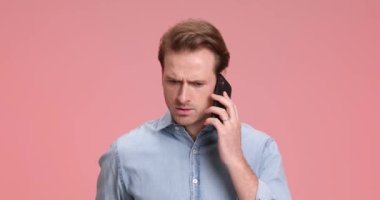 Kot gömlekli endişeli bir genç adam telefonda konuşuyor. Pembe arka plandaki zor bir sorunu çözmenin yollarını düşünürken endişeli bir şekilde yüzünü ovuyor.