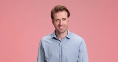 Kot gömlekli yakışıklı genç manken stüdyoda pembe arka planda yürürken parmak uçlarına ve askeriyeye selam veriyor.