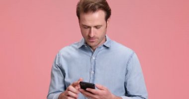 Mavi kot gömlekli yakışıklı manken telefona cevap veriyor ve iyi bir sohbet ediyor, stüdyoda pembe arka planda gülüyor ve poz veriyor.