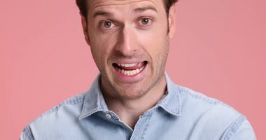 Kot gömlekli komik çekici bir adam eğleniyor, şapşal gibi davranıyor, aptalca suratlar yapıyor, stüdyoda pembe arka planda gülüyor ve gülüyor.