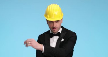 Yakışıklı iş adamı poz veriyor, kollarını kavuşturuyor, kaskını, papyonunu ve smokinini tamir ediyor.