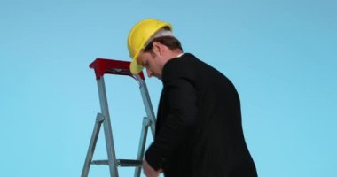 İnşaat mühendisi merdivenden iniyor, ceketini kapatıyor, kupasına bakıyor ve başarısını kutluyor.