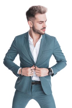 Seksi sakallı genç iş adamı beyaz arka planda poz verirken takım elbisesinin düğmelerini açmaya çalışıyor.