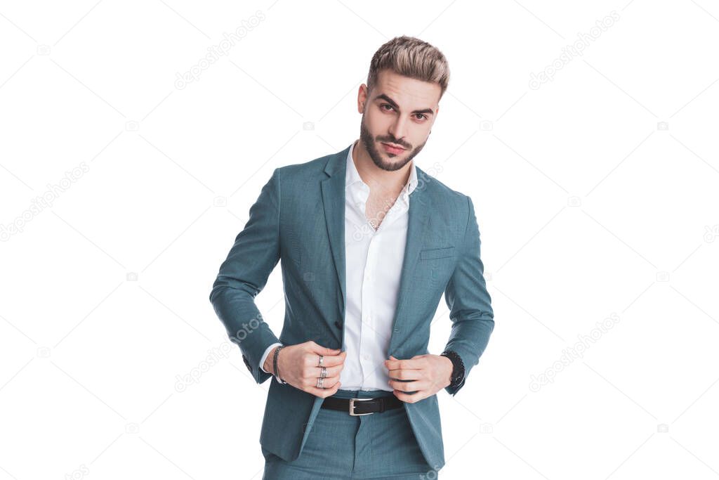 portrait of attractive young guy with untied shirt buttoning suit and smiling while standing isolated on white background in studio