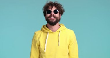 Sarı kapüşonlu bipolar genç adam nöbet geçiriyor ve gülmeye başlıyor, gözlüklerini alıyor ve mavi arka planda şakalaşıyor.