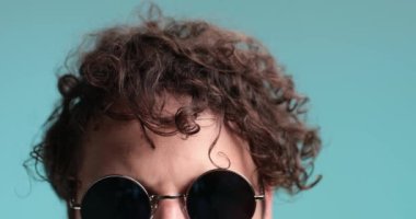 Gözlük gösteren, şaşıran, geri çekilip korkan, gülen ve mavi arka planda eğlenen havalı, tıraşsız hipster 'ı yakından çek.