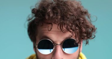 Kıvırcık saçlı adam kameraya yaklaşıyor, geri çekiliyor ve korkuyor, eğleniyor ve gülüyor.