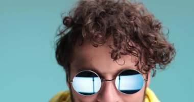 Havalı, genç, sıradan bir hippi. Geri çekiliyor ve yavaş çekimde ellerini hareket ettiriyor. Stüdyoda eğleniyor ve mavi arka planda mutlu oluyor.