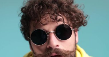 Uzun sakallı kıvırcık saçlı adamın yavaş çekimde arkada hareket ettiğini, çığlık attığını, elleriyle dinamik hareketler yaptığını, çerçevelediğini ve stüdyoda mavi arka planda eğlendiğini.