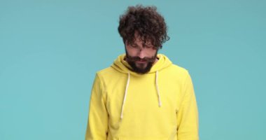 Bıyıklı batıl inançlı adam yukarı bakıyor, şans diliyor, hevesli suratlar yapıyor ve stüdyoda mavi arka planda gülümsüyor.