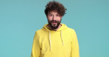 Hevesli havalı hippi sarı kazaklı, şaşırmış bir yüz ifadesi takınıyor, ağzını açıyor ve stüdyoda mavi arka planda yumruğunu havaya kaldırarak iyi haberi kutluyor.
